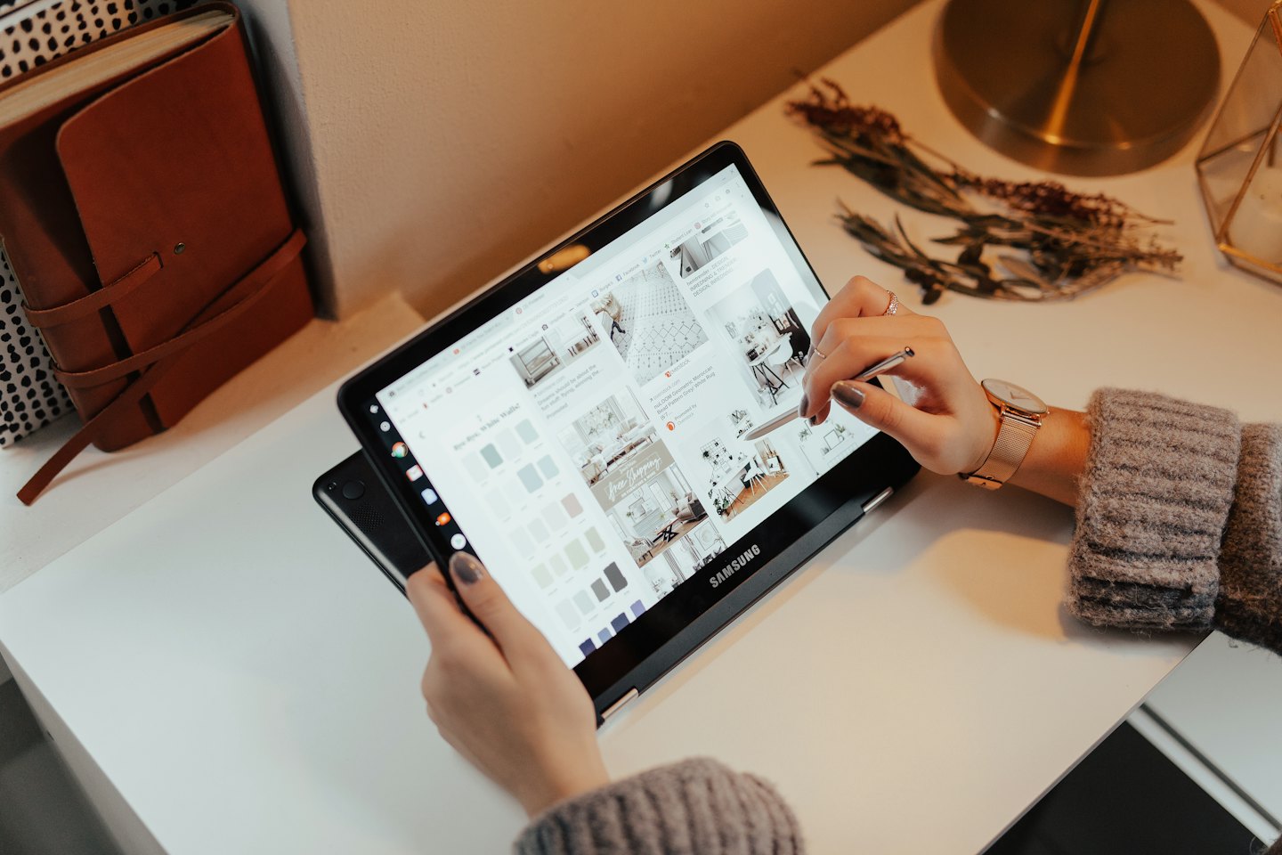 Hände, die ein Tablet auf einem weißen Schreibtisch mit Deko-Inspiration benutzen.